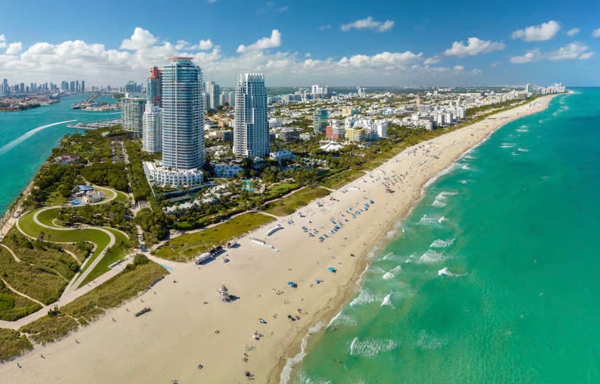 Aerial view of South Beach, Miami, with high-rise condominium towers beside a wide sandy beach and turquoise ocean