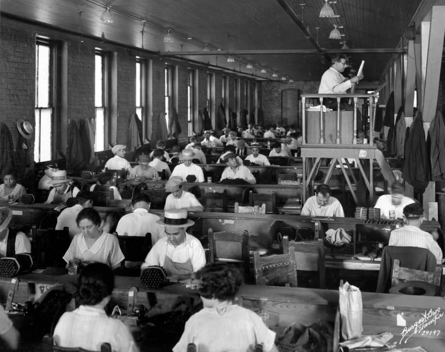 Rows of cigar workers at their benches as a lector reads aloud from a raised platform, Tampa, 1929