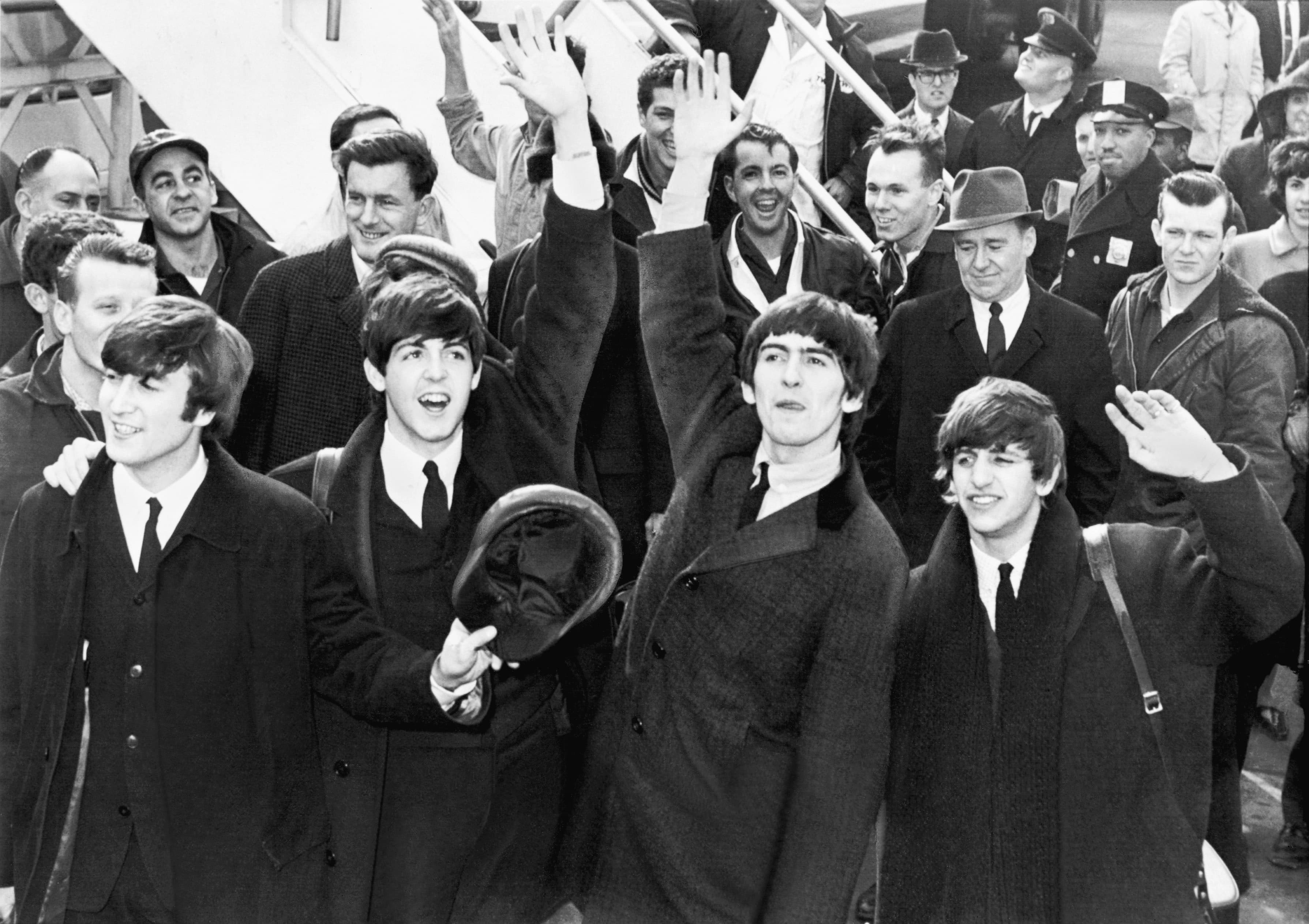 The Beatles wave to a crowd of fans from the top of airplane stairs after landing in New York in February 1964.