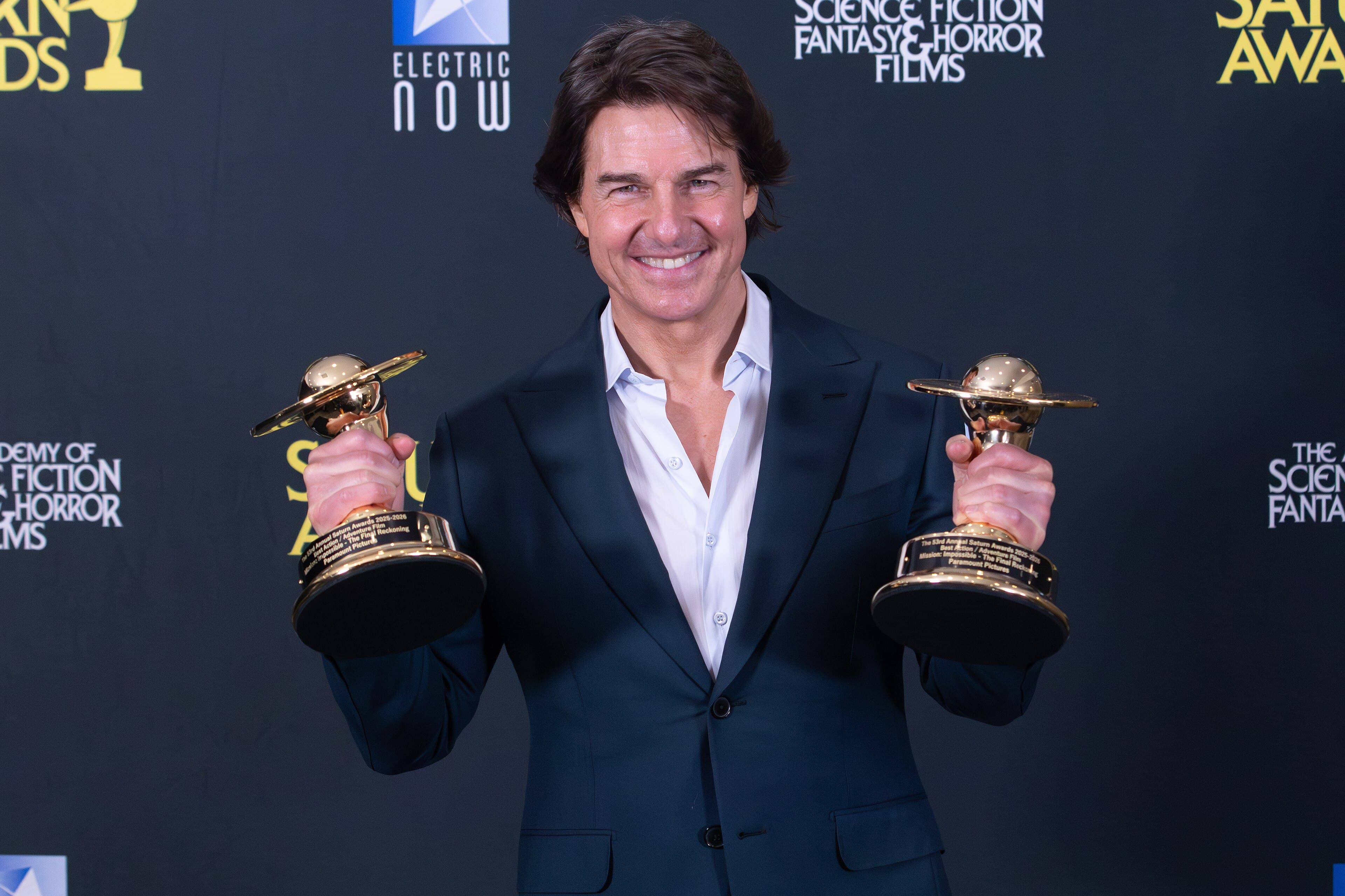 Tom Cruise smiling and holding two awards at the 2026 Saturn Awards in Los Angeles