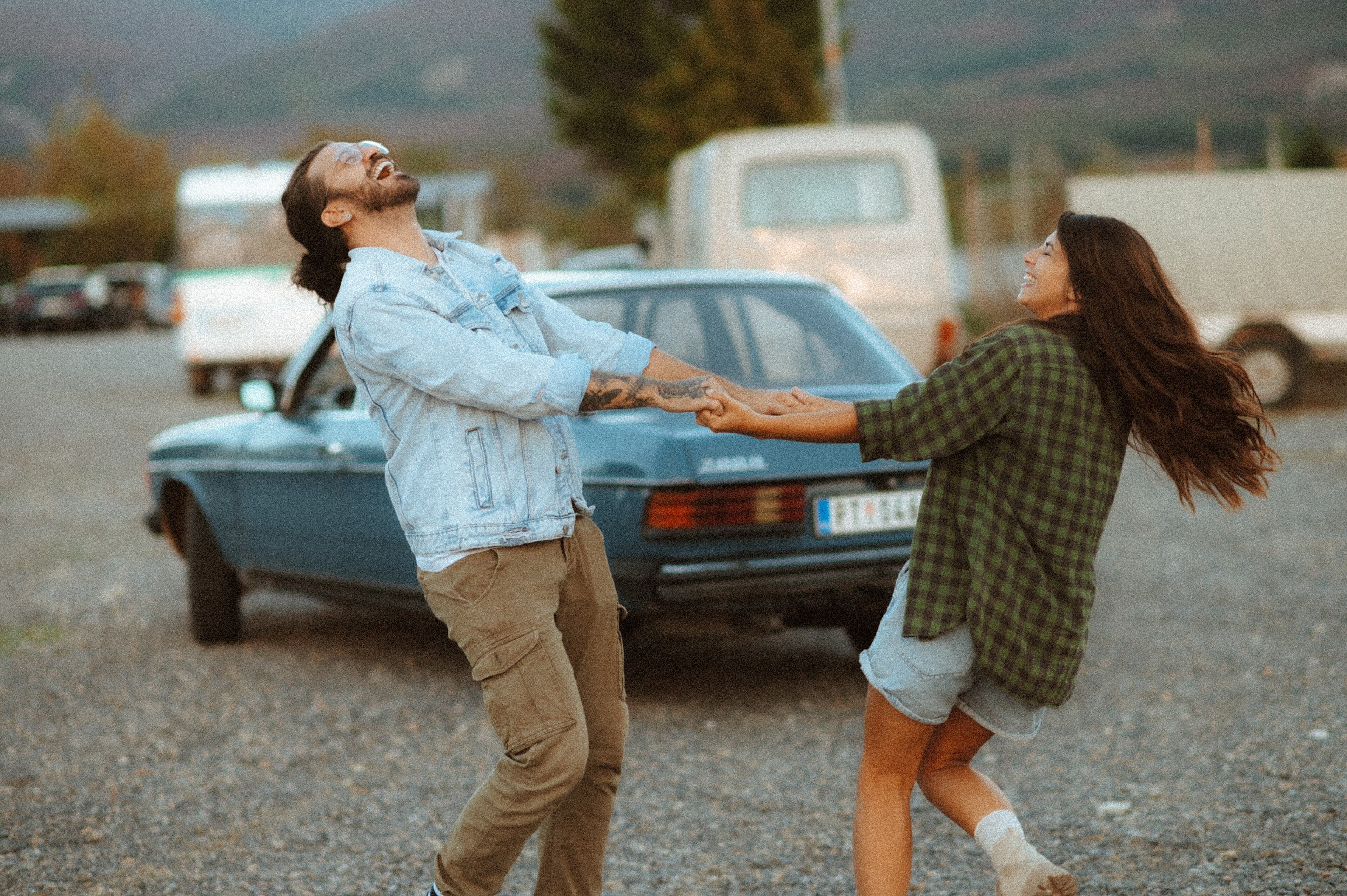 A man and a woman laughing as they spin around together in a parking lot at sunset